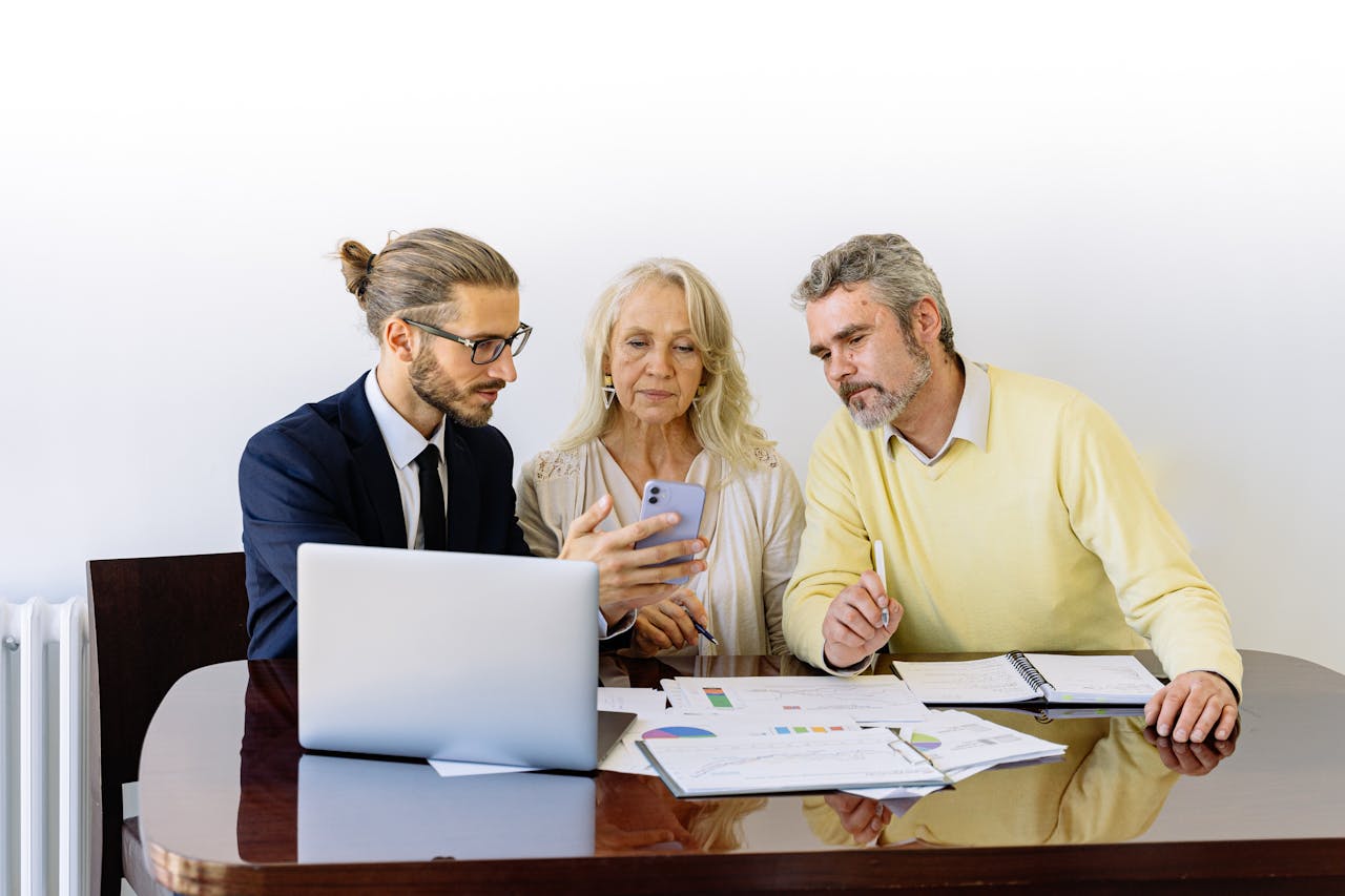 Three individuals collaborating on financial documents during a business meeting.